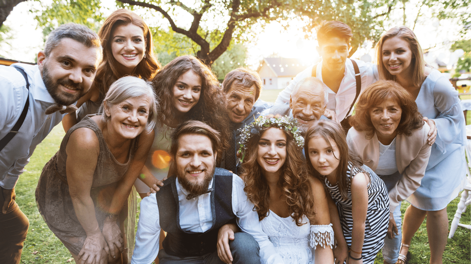 A joyful group photo of a wedding party outdoors, featuring the bride and groom surrounded by family and friends.
