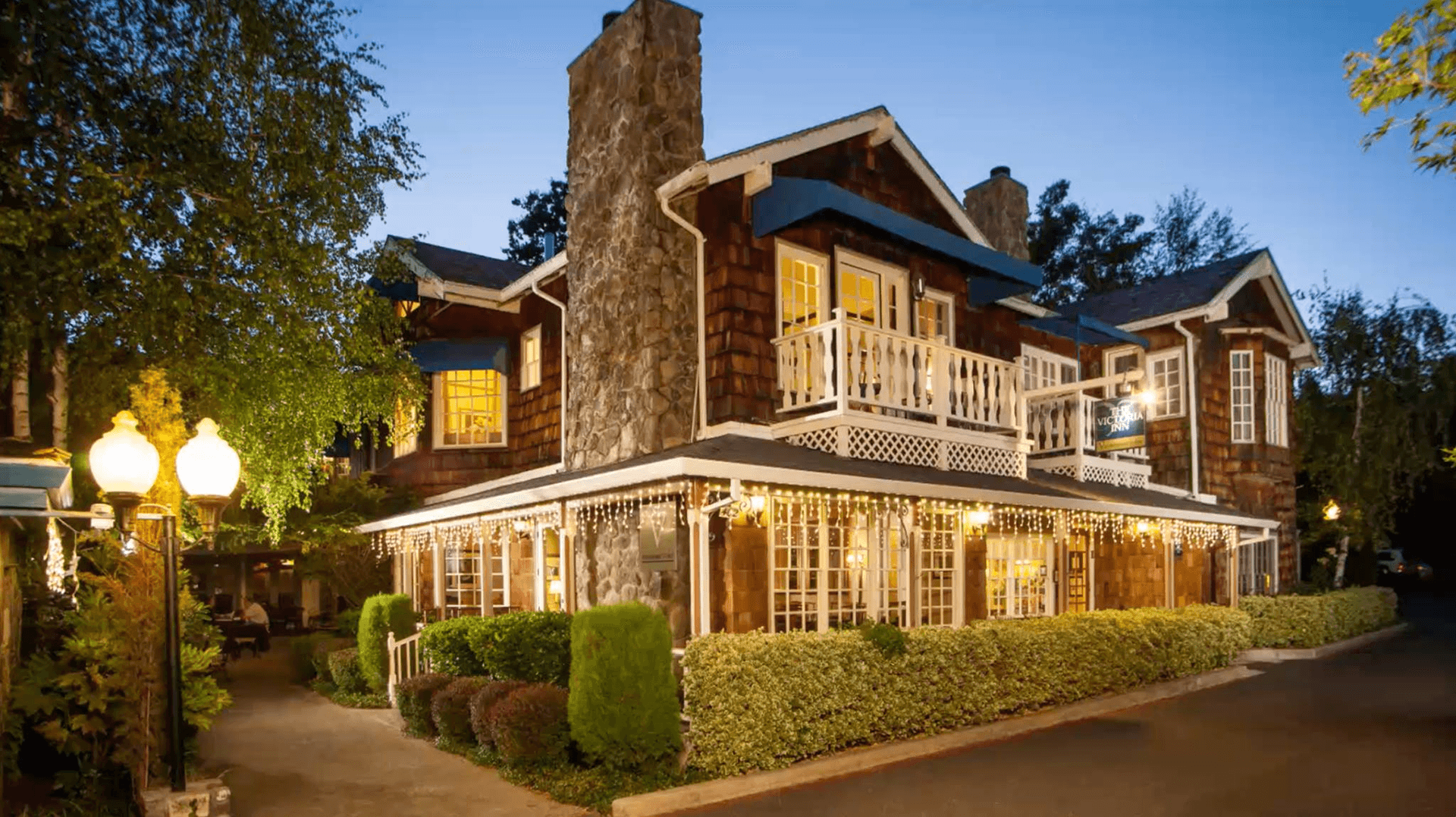 A charming two-story house with stone accents, surrounded by lush greenery and soft lighting at dusk.