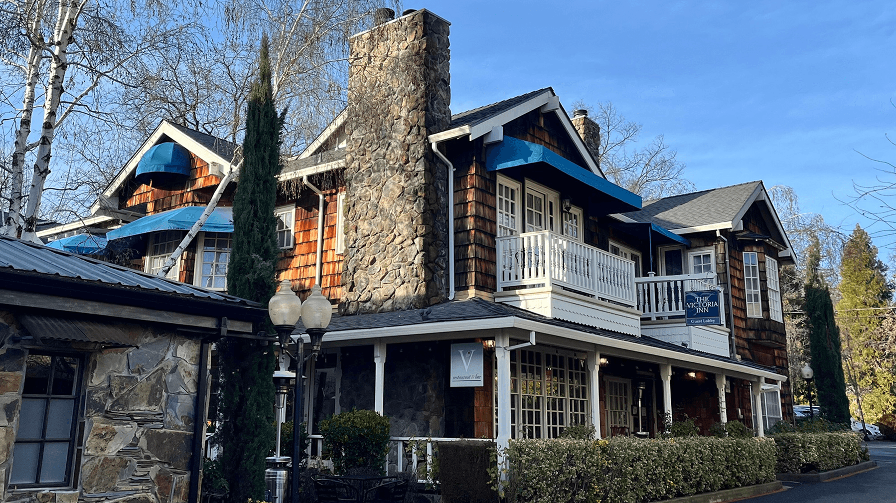 A charming wooden and stone building with a balcony and blue awnings surrounded by trees.