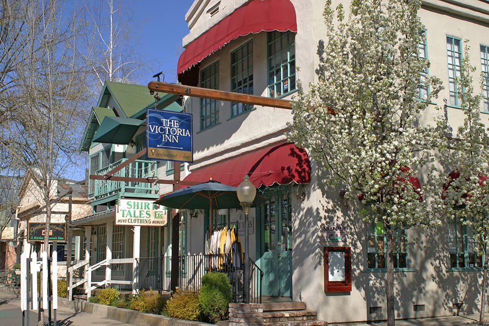 A quaint inn with a red awning and nearby shops, surrounded by blooming trees.