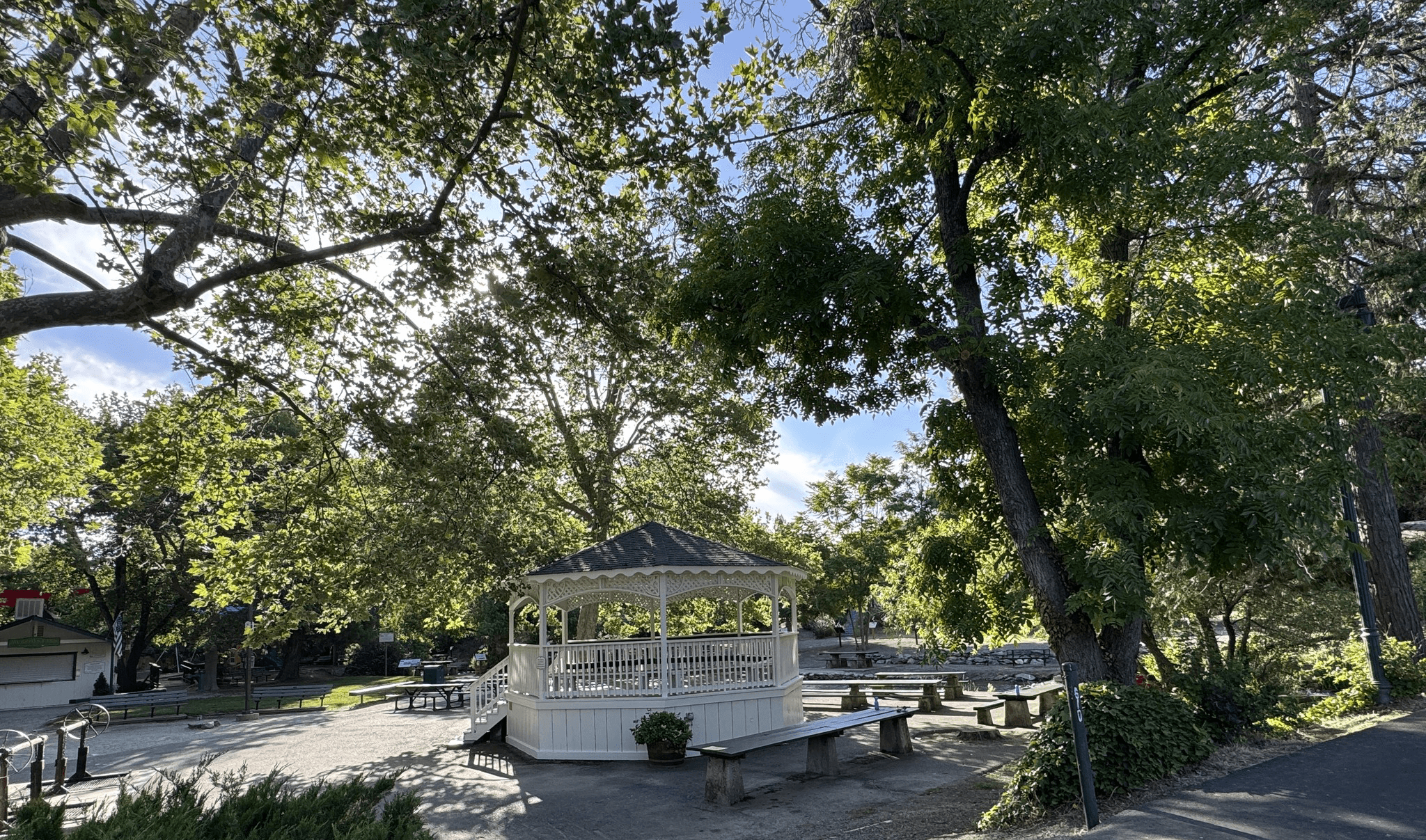 A white gazebo surrounded by lush greenery and benches in a park.